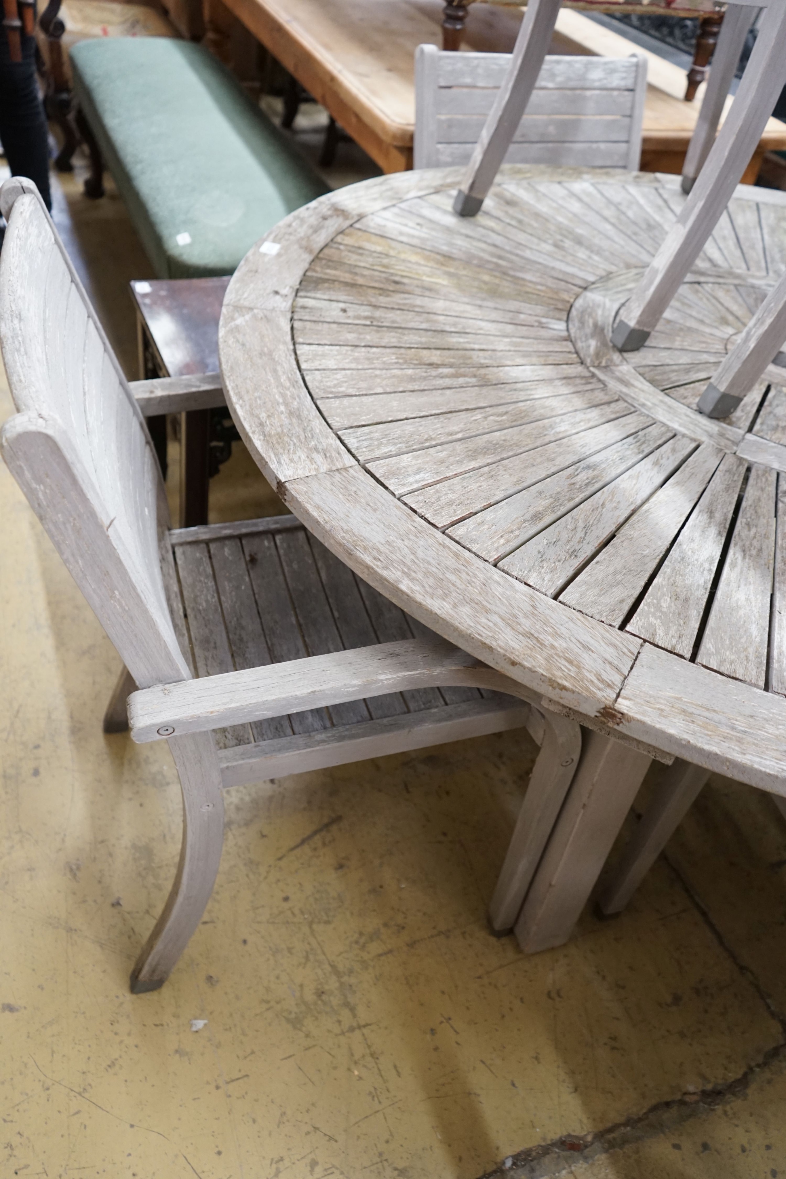 A circular weathered teak garden table, diameter 153cm, height 75cm together with six weathered teak stacking garden elbow chairs